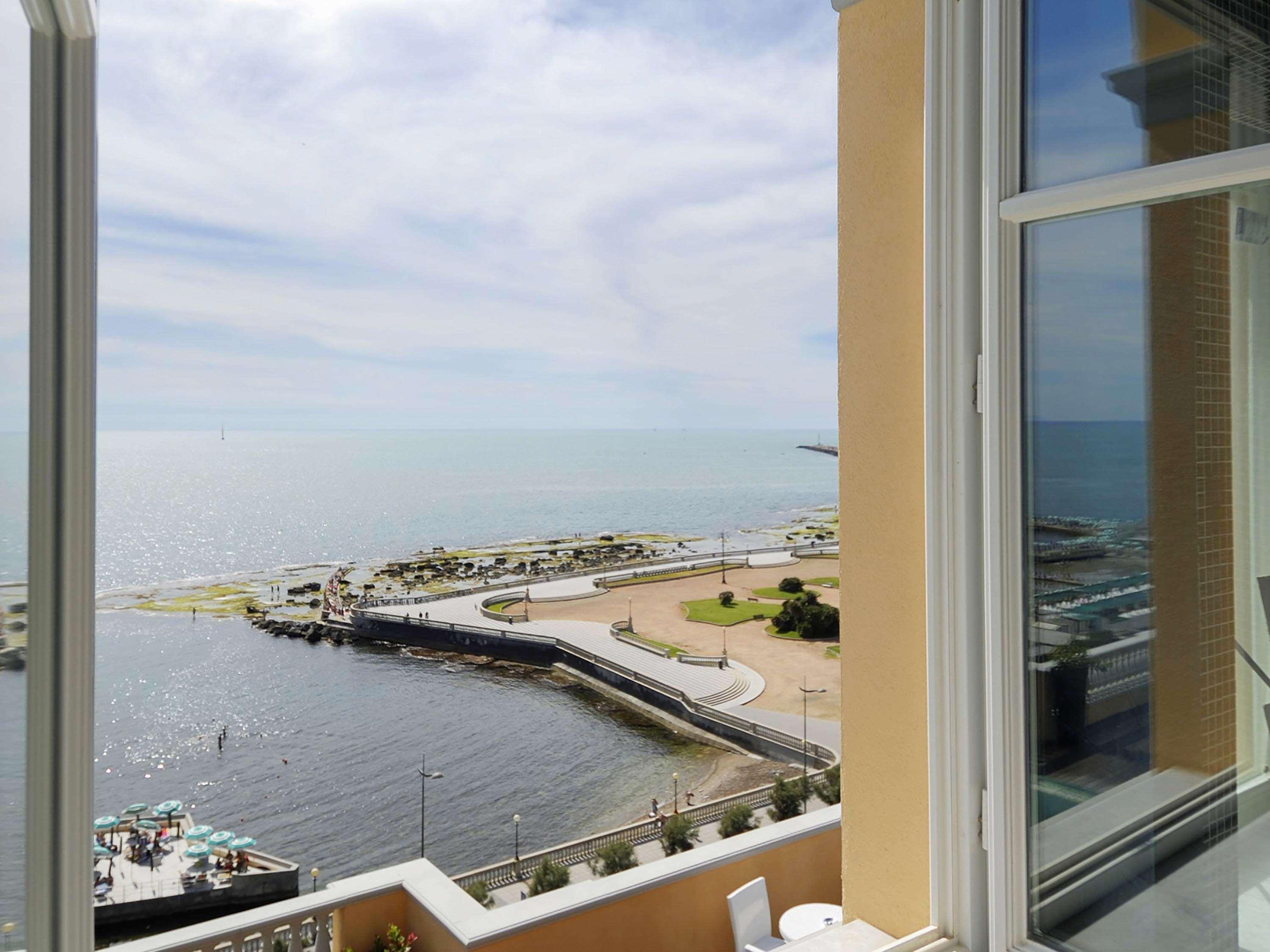 Grand Hotel Palazzo Livorno MGallery Collection Esterno foto The photo shows a view from a window overlooking a calm, expansive body of water. In the foreground, there's a harbor or dock area with a curved pier extending out into the water. There are likely boats or small vessels visible near the dock. The sho