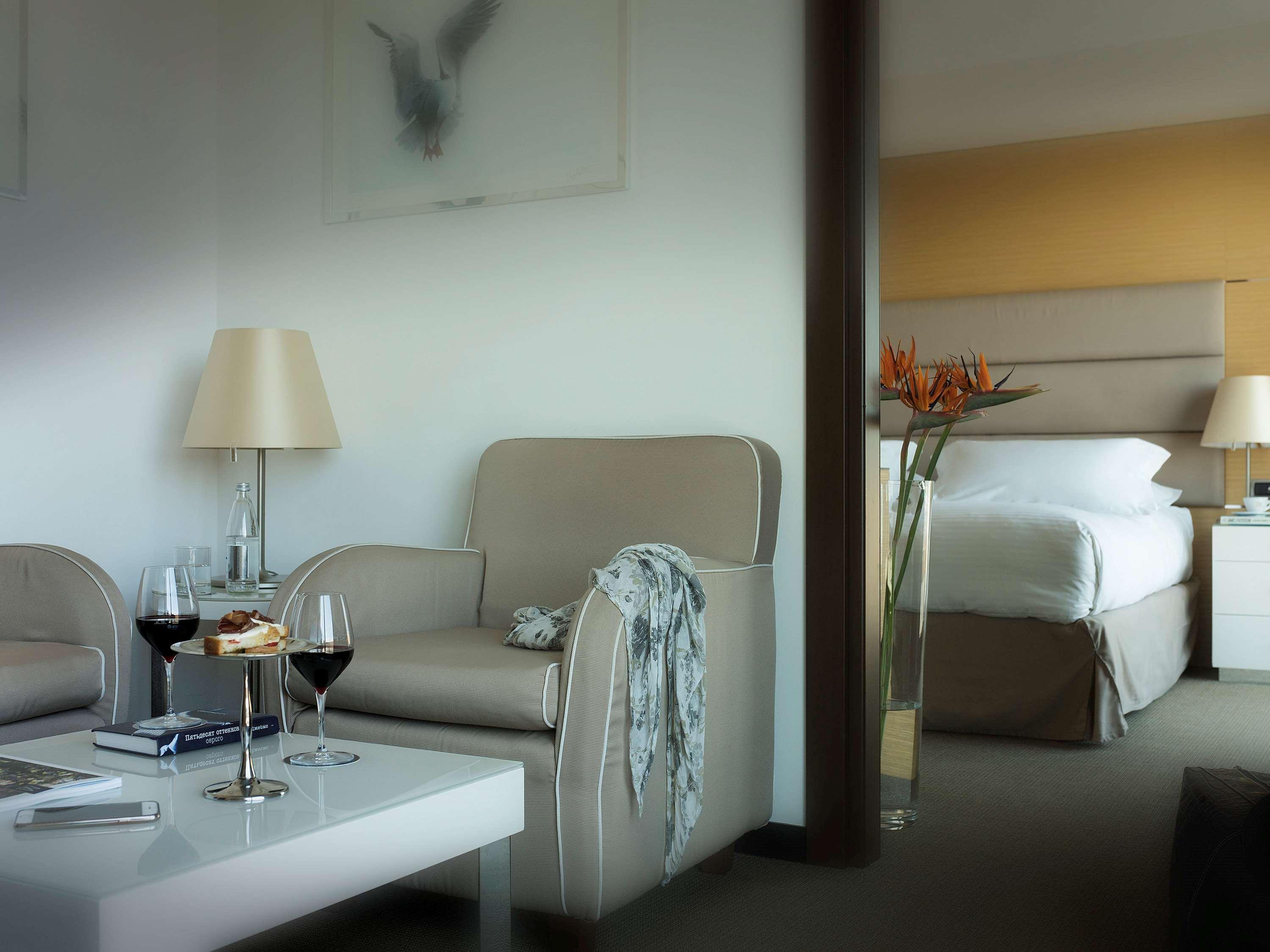 Grand Hotel Palazzo Livorno MGallery Collection Esterno foto The photo shows a modern hotel room or suite. On one side, there is a cozy seating area with two light-colored chairs and a small coffee table. On the table, there are two glasses of red wine and a plate of cookies, suggesting a relaxing atmosphere. 