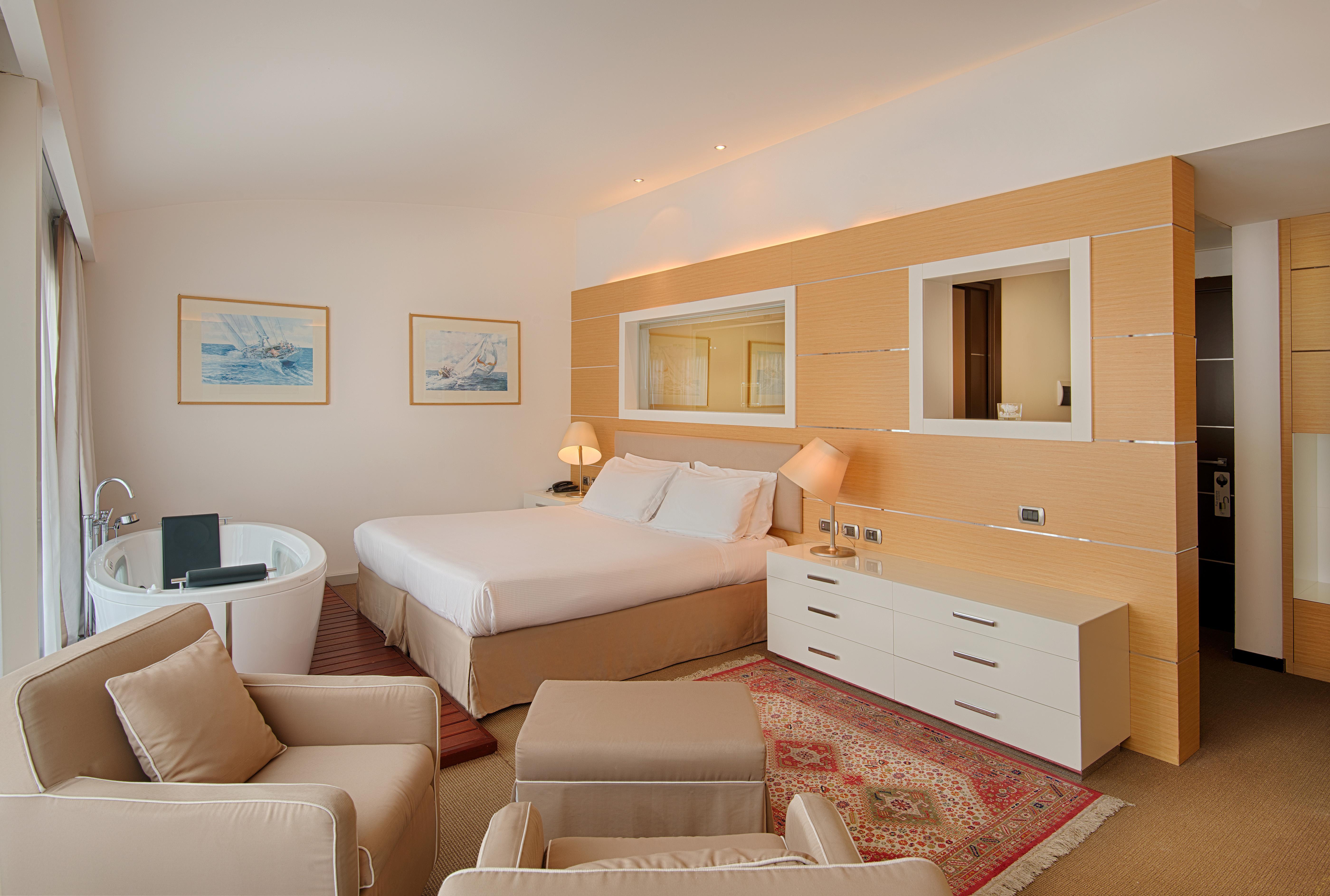 Grand Hotel Palazzo Livorno MGallery Collection Esterno foto The photo shows a modern hotel room. It features a large bed with white bedding, flanked by bedside lamps. There are two armchairs and a small coffee table, creating a cozy seating area. A stylish bathtub is visible to the left, and the room has ligh