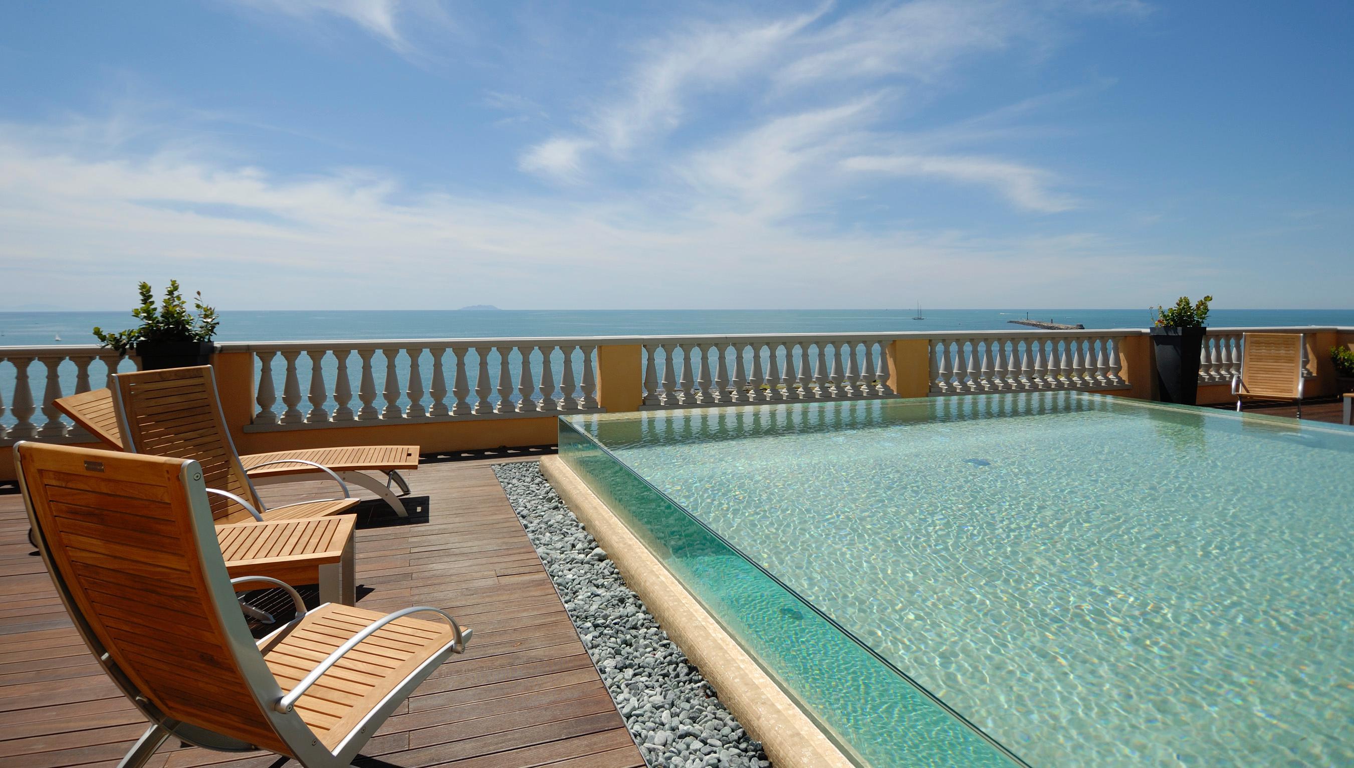 Grand Hotel Palazzo Livorno MGallery Collection Esterno foto The photo depicts a serene outdoor setting featuring an infinity pool that appears to merge with the horizon. The pool has a glass edge, enhancing the illusion of continuity with the ocean beyond. Surrounding the pool are wooden lounge chairs, positi