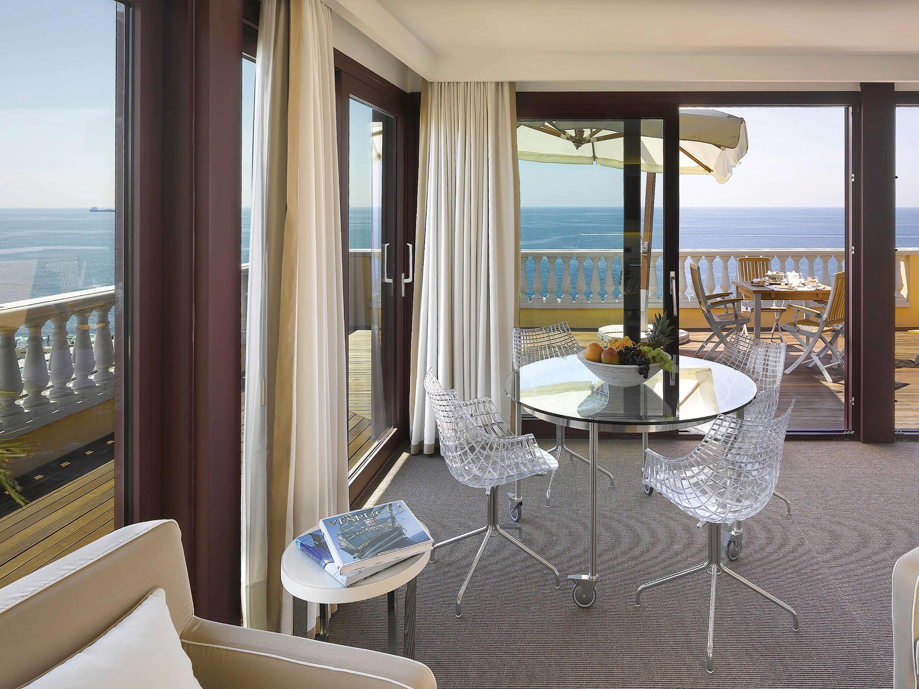 Grand Hotel Palazzo Livorno MGallery Collection Esterno foto The photo depicts a modern interior space, likely a hotel suite or a luxury apartment. It features large glass doors that open onto a balcony, offering a view of the ocean. The room has neutral-toned furnishings, including a cozy sofa. A circular gla