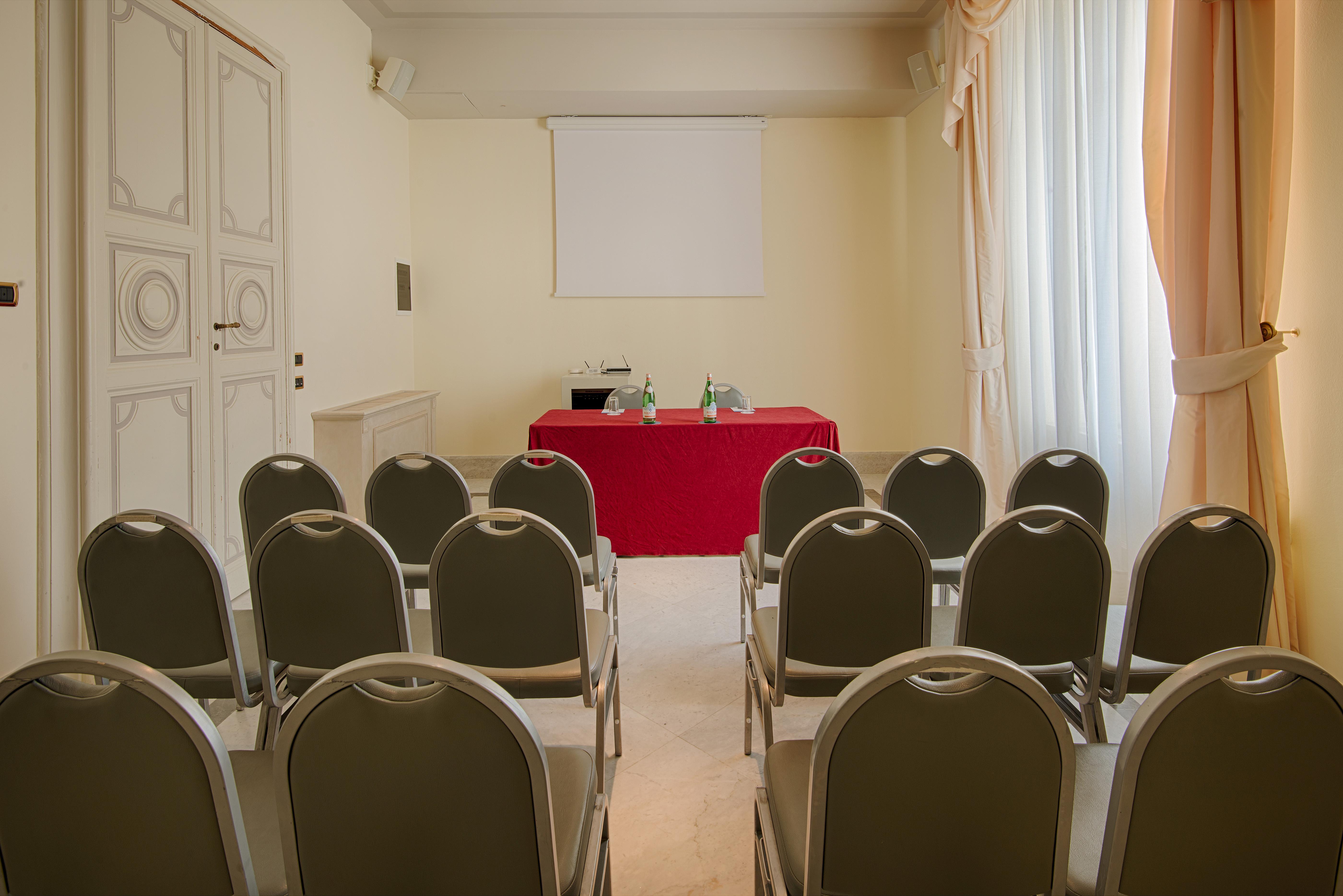 Grand Hotel Palazzo Livorno MGallery Collection Esterno foto The photo shows a small meeting room set up for an event or presentation. There are several gray chairs arranged in rows facing a table covered with a red cloth. The table has some decorative items, possibly plants or flowers. In the background, ther