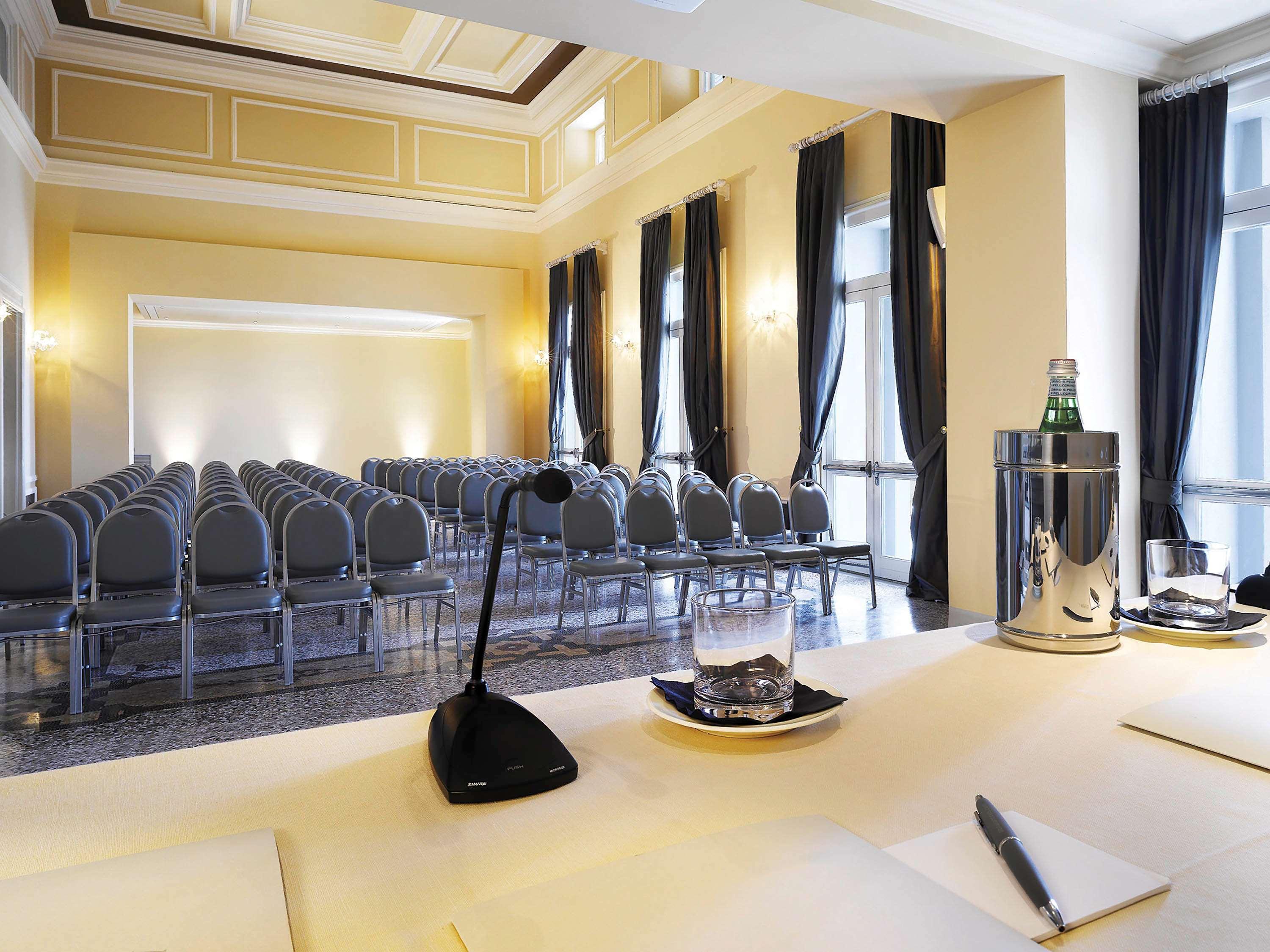 Grand Hotel Palazzo Livorno MGallery Collection Esterno foto The photo shows a conference or meeting room. In the foreground, there is a table with a microphone, a glass, and a bottle in a cooler. There are also some notepads and pens on the table. In the background, there is a seating arrangement with several
