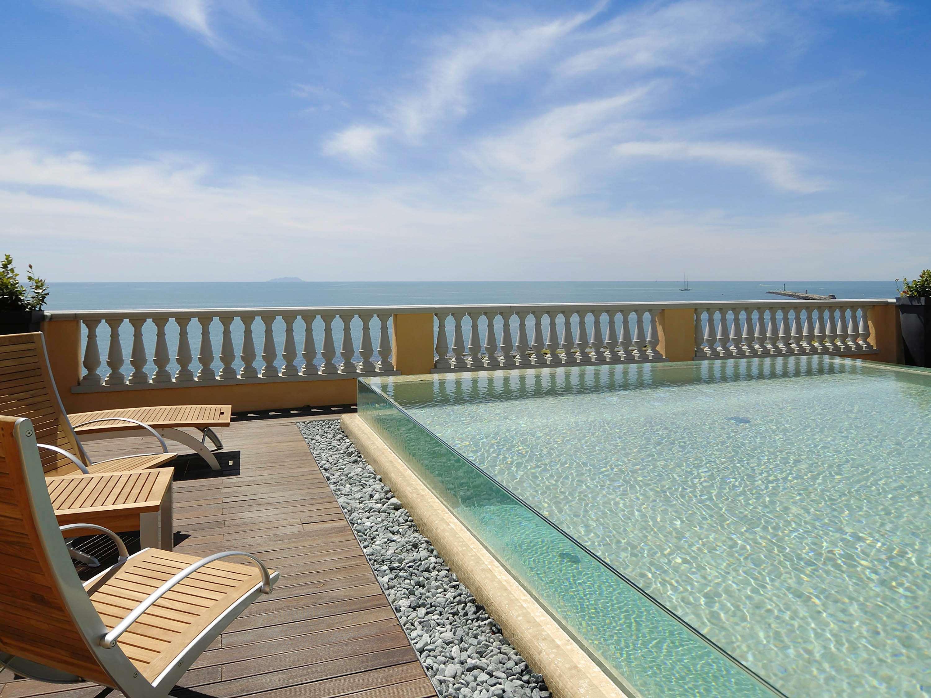 Grand Hotel Palazzo Livorno MGallery Collection Esterno foto The photo shows a tranquil outdoor setting featuring a swimming pool that appears to have an infinity edge, giving an illusion of merging with the ocean in the background. There are a few wooden lounge chairs positioned alongside the pool on a wooden