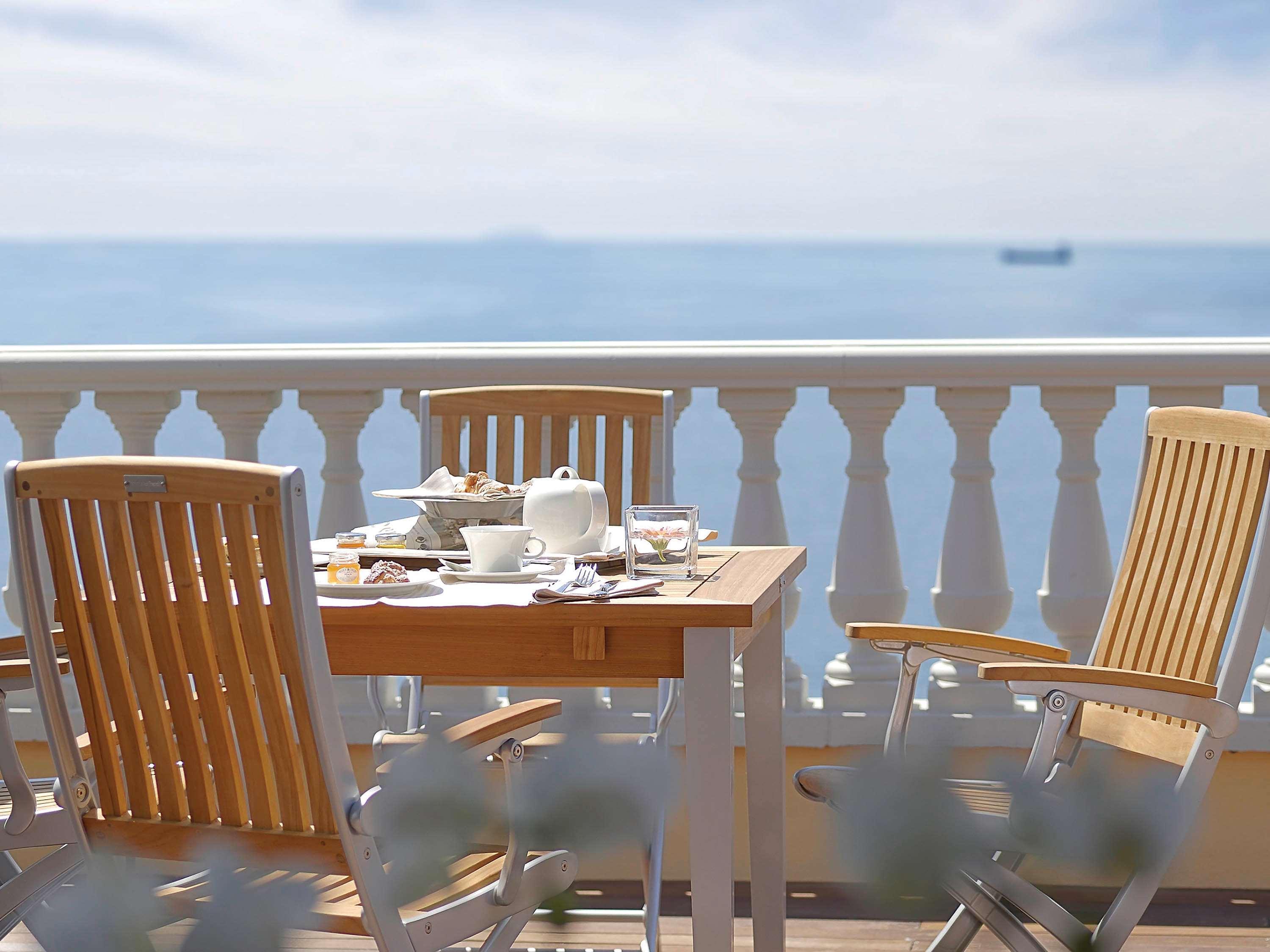 Grand Hotel Palazzo Livorno MGallery Collection Esterno foto The photo shows a beautiful outdoor setting, likely a balcony or terrace overlooking a calm sea. There is a wooden table with a light breakfast spread, including a tea set and some food items. Two comfortable wooden chairs are positioned around the t