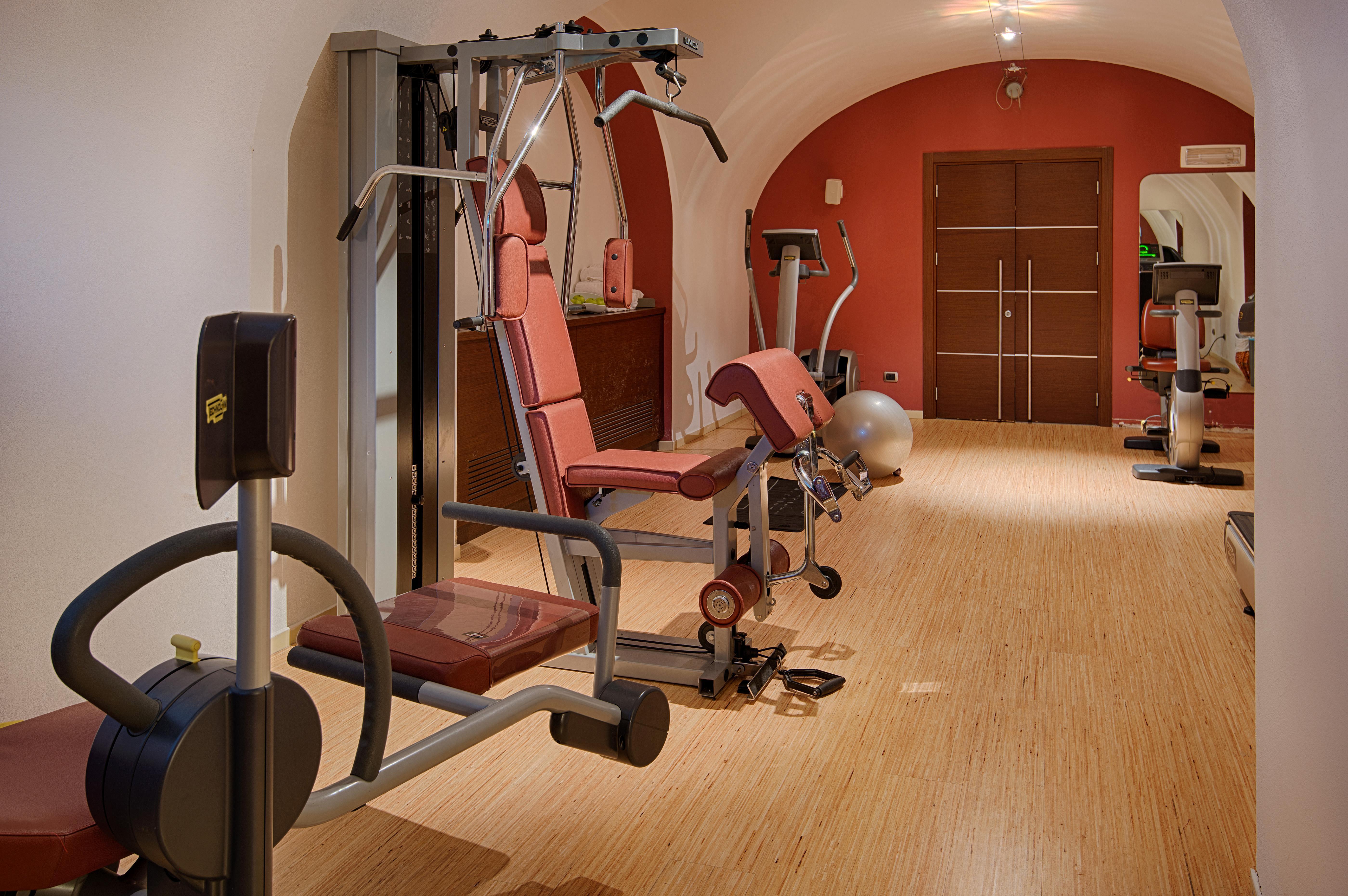 Grand Hotel Palazzo Livorno MGallery Collection Esterno foto The photo shows a fitness area equipped with exercise machines. The room features a warm color scheme, with walls painted in shades of red. There are various gym equipment pieces, including weight machines and a stationary bike. The flooring is made 