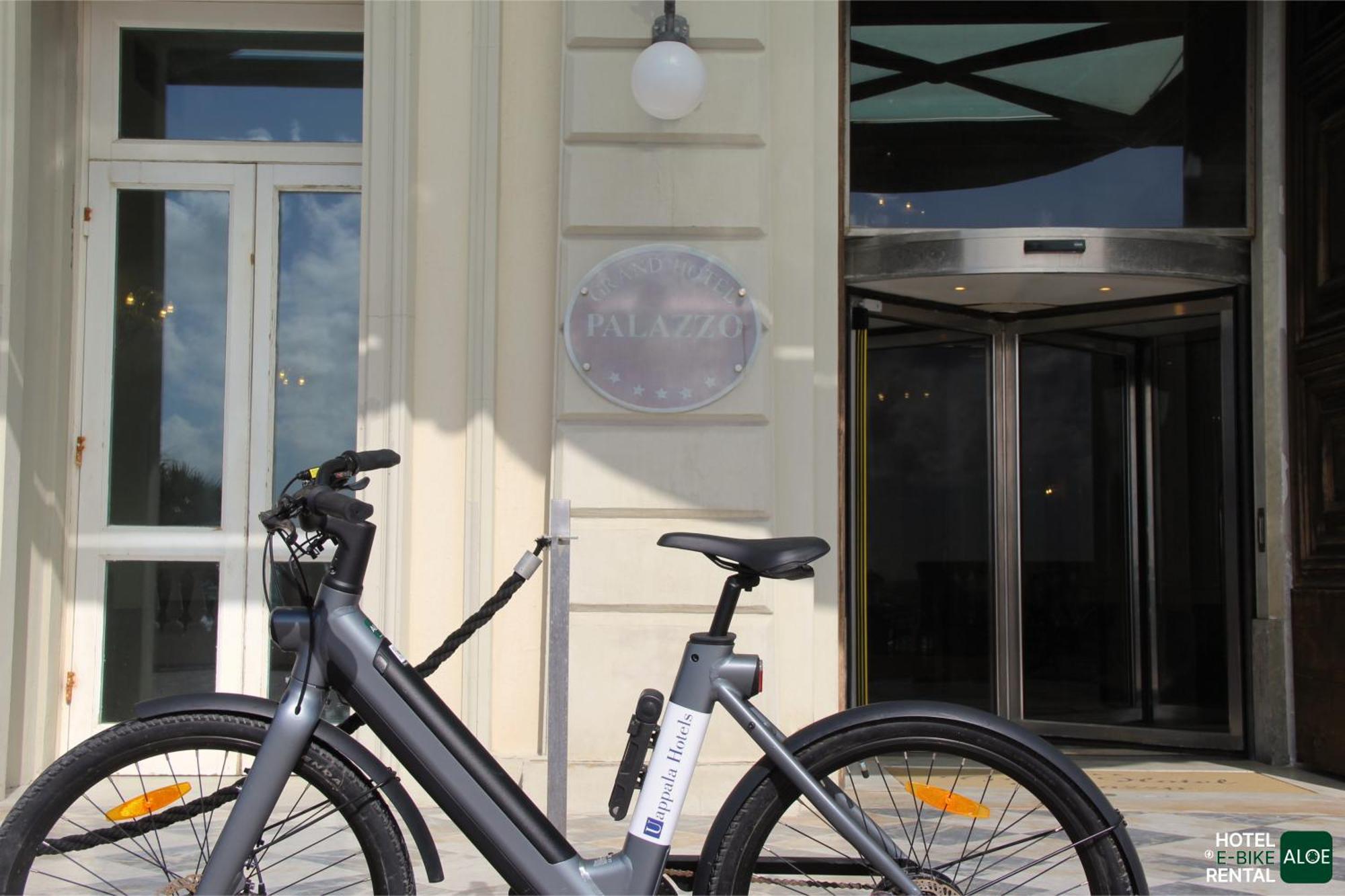 Grand Hotel Palazzo Livorno MGallery Collection Esterno foto The photo shows an electric bike parked in front of an entrance to a building. The doorway features a revolving glass door and a decorative sign that appears to indicate the name of the establishment. The building's facade is light-colored, and there