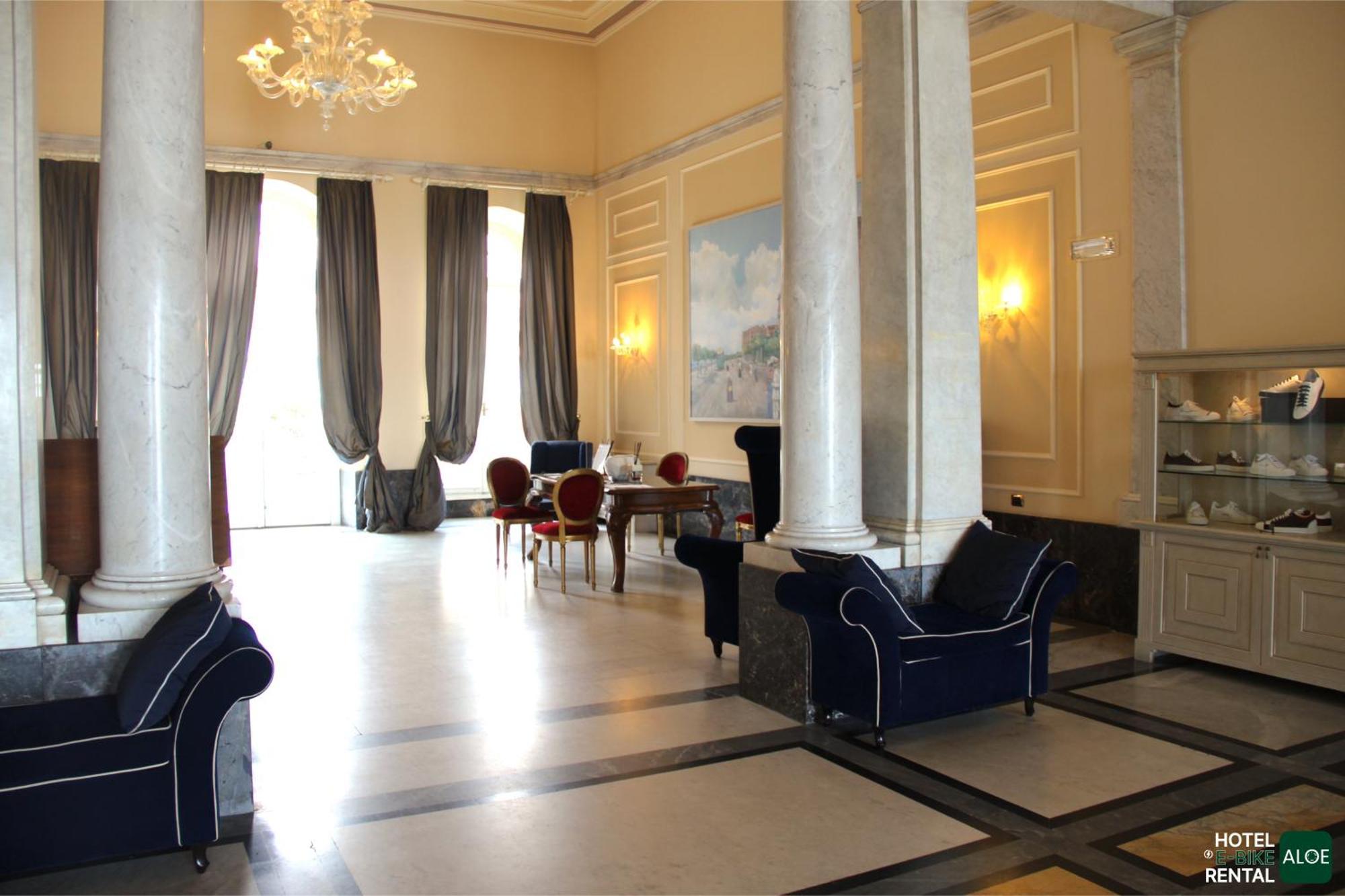Grand Hotel Palazzo Livorno MGallery Collection Esterno foto The photo displays a spacious and elegantly designed interior, likely part of a hotel or a formal venue. The room features tall ceilings, large windows with flowing drapes, and marble-like flooring. 

In the center, there is a dining or meeting area 