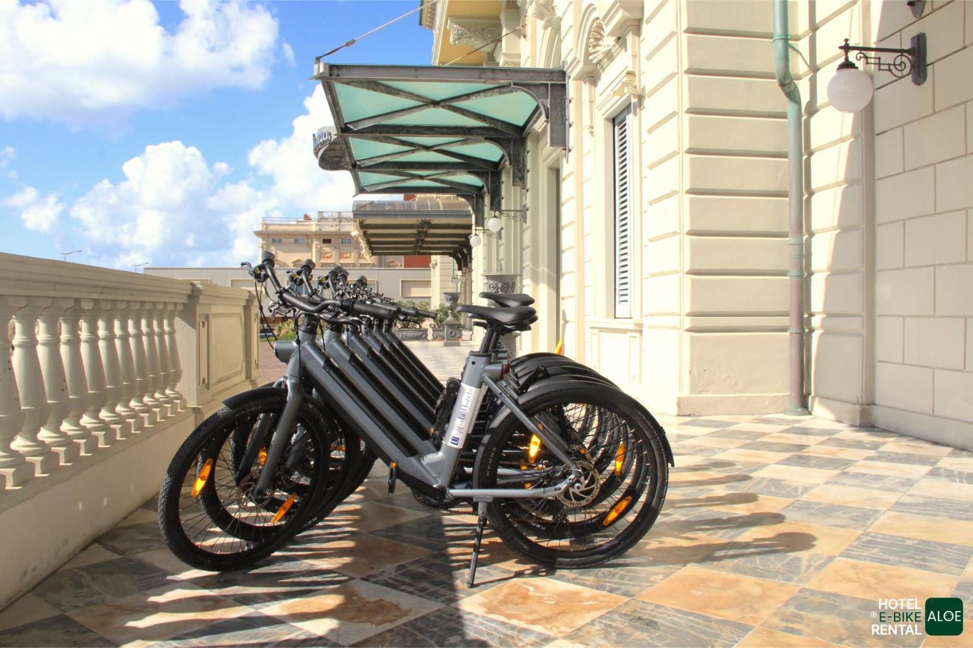 Grand Hotel Palazzo Livorno MGallery Collection Esterno foto The photo shows a row of electric bicycles lined up on a paved surface outside a building with a classic architectural style. The e-bikes are predominantly black and are parked near a balcony with large windows. In the background, there are blue skie