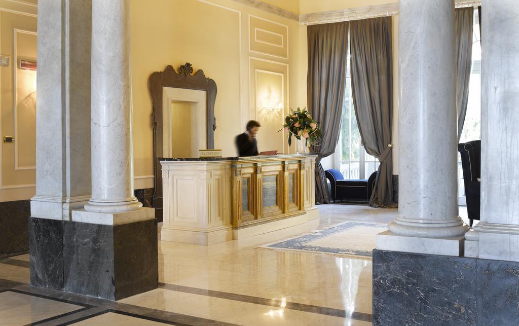 Grand Hotel Palazzo Livorno MGallery Collection Esterno foto The photo shows a luxurious hotel lobby. In the foreground, there is an elegant reception desk made of light-colored wood with golden accents. Behind the desk, a staff member is busy attending to tasks. To the sides, there are marble columns supporti